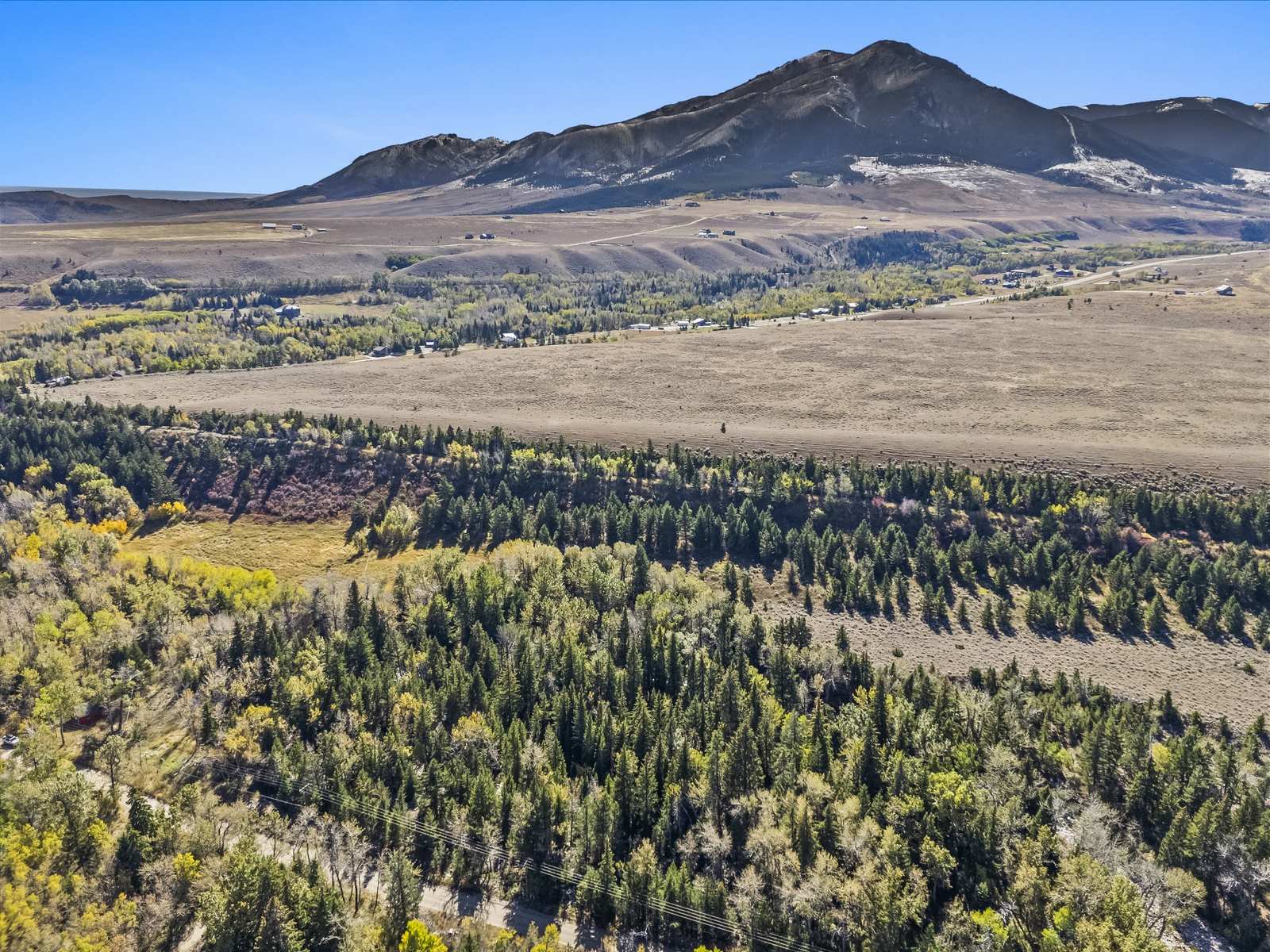 Drone view of a treed creek bottom and hay meadow below the mountains near Red Lodge, Montana