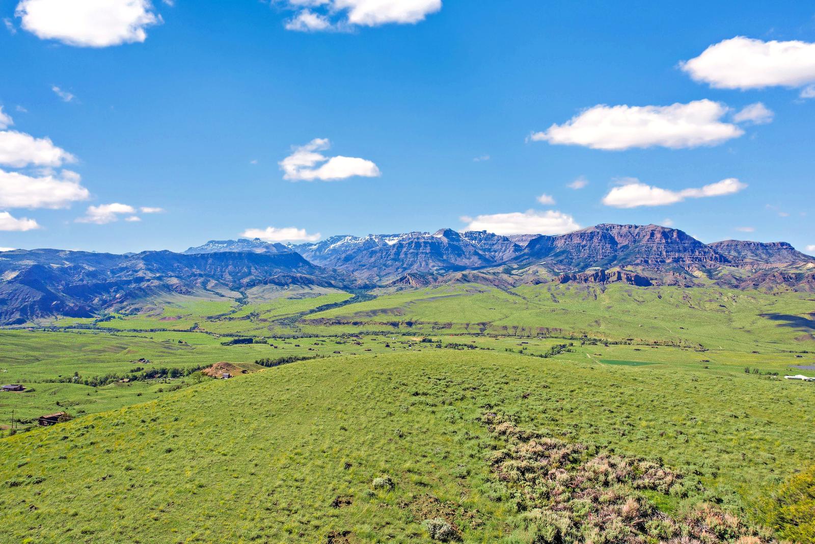 Rolling green hills below a long mountain range, Montana land we've worked on
