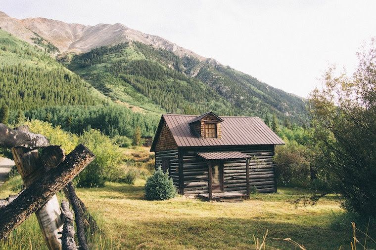 Log cabin with a metal roof in a mountain meadow below forested slopes